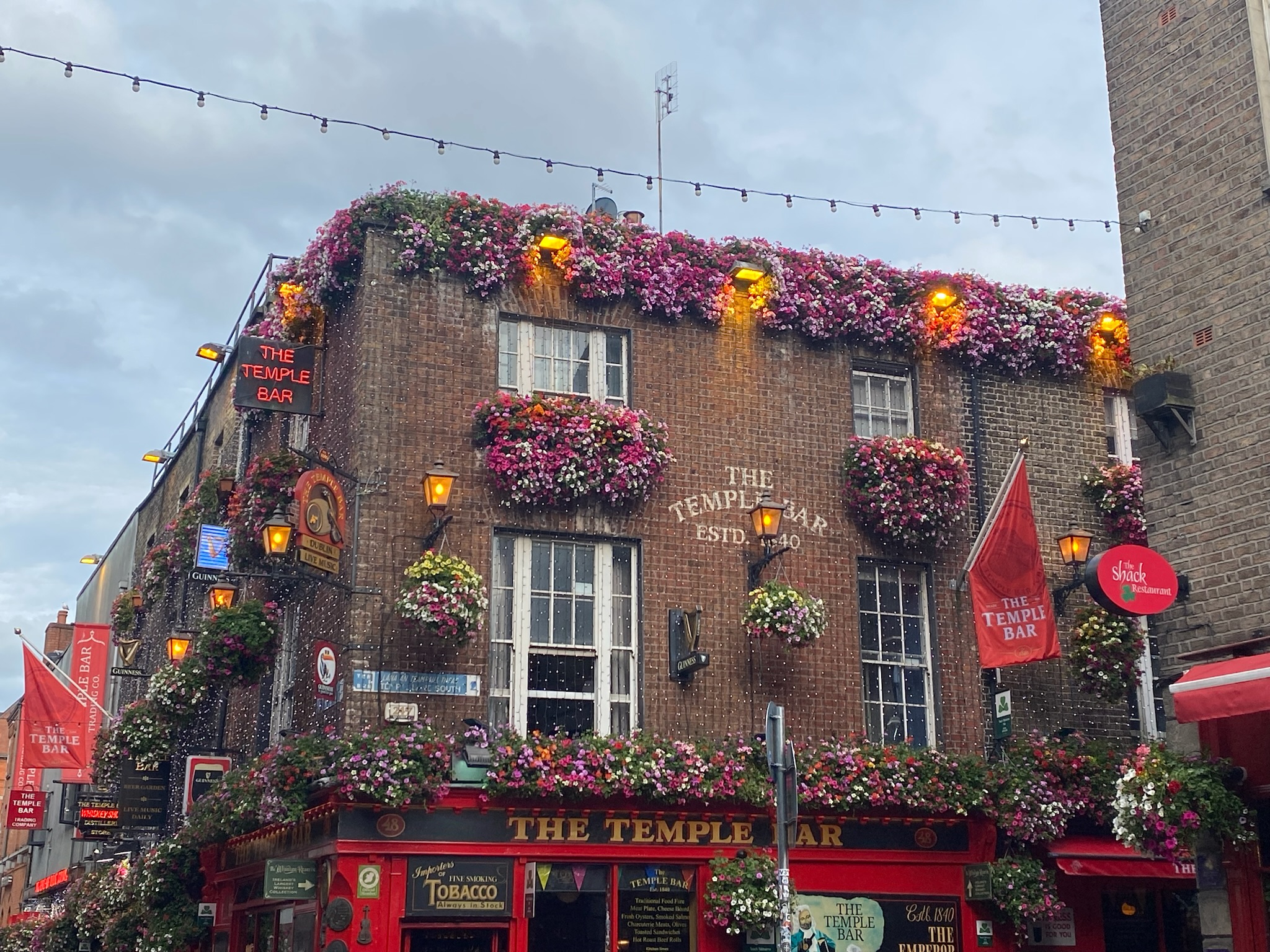 Photo of Temple Bar in Dublin Ireland. A brick building, with lights and flowers dangling from the window sills.